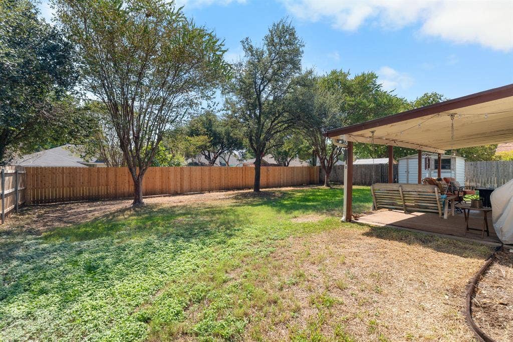 10712 Apache Drive, Waco, TX 76712 Expansive backyard oasis featuring mature shade trees, lush lawn, and a covered patio structure with wood-beam construction