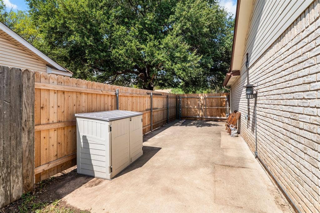 10712 Apache Drive, Waco, TX 76712 Outdoor concrete patio space featuring a wood fence, brick exterior siding, and an exterior light fixture