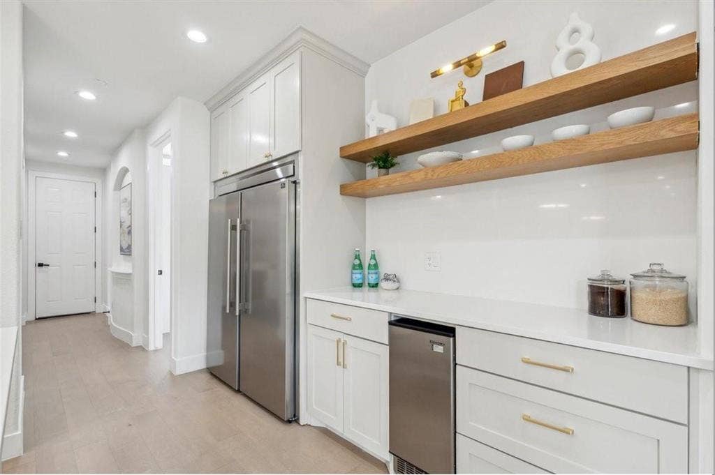 1750 Greenwood Court, Prosper, TX 75078 White cabinetry with gold-tone hardware, stainless steel refrigerator, built-in beverage cooler, white countertop, and wood-finish open shelving