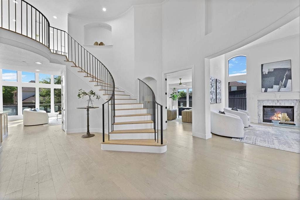 1750 Greenwood Court, Prosper, TX 75078 Grand curved staircase with wrought iron balusters, high ceilings, large arched windows, wood-finish flooring, and a fireplace with a decorative mantel