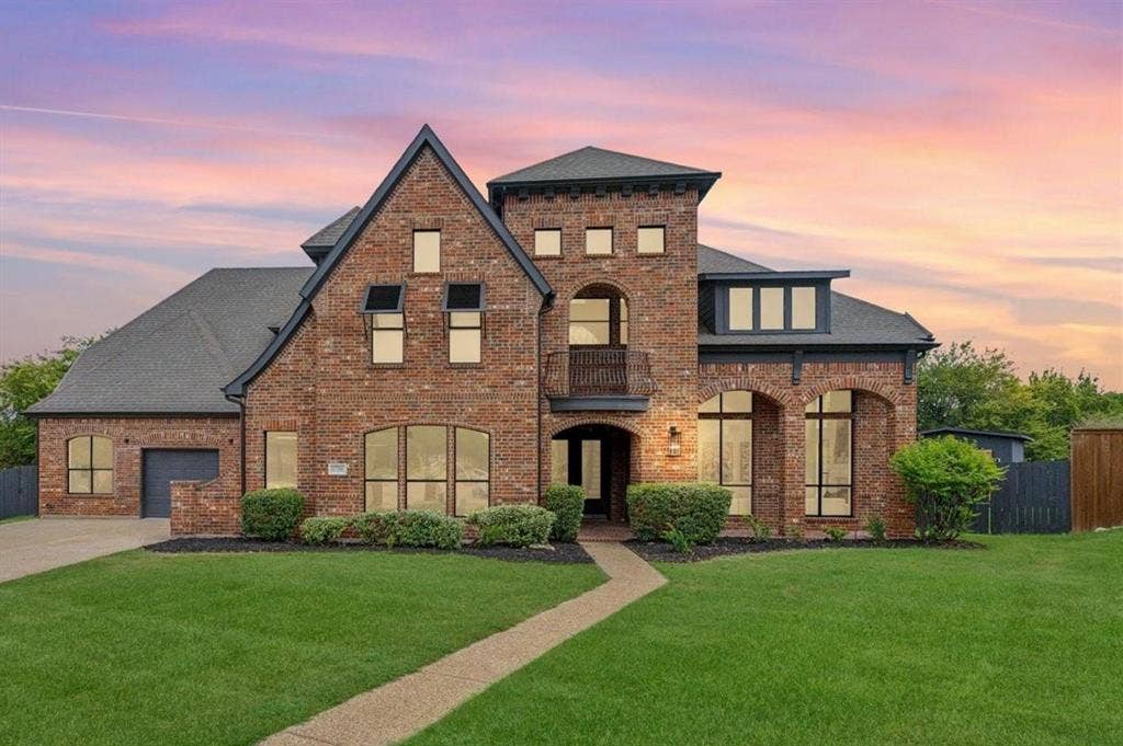 1750 Greenwood Court, Prosper, TX 75078 Brick exterior with dark gray roofing, an integrated garage, a second-story balcony, and arched window details
