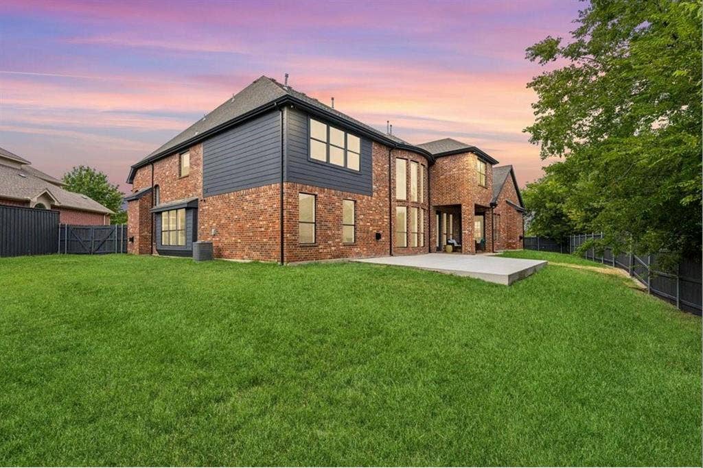 1750 Greenwood Court, Prosper, TX 75078 Expansive green lawn with a concrete patio, brick exterior with dark siding, and large windows