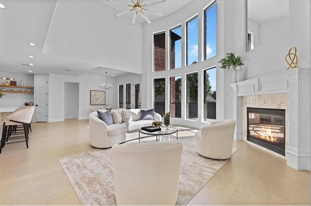 1750 Greenwood Court, Prosper, TX 75078 Double-height ceiling, floor-to-ceiling windows, wood-finish flooring, built-in fireplace with stone surround, and a ceiling fan with integrated lighting