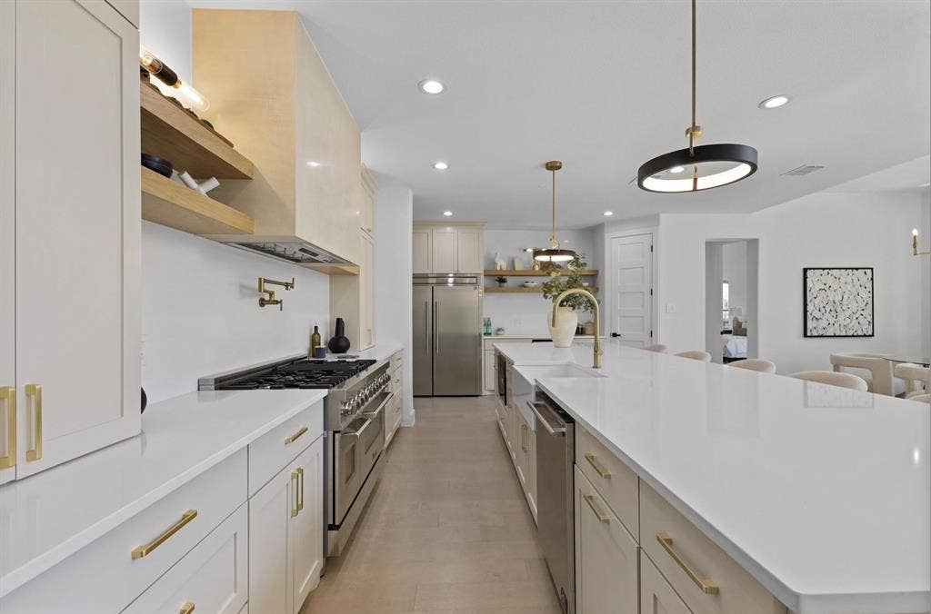 1750 Greenwood Court, Prosper, TX 75078 Expansive kitchen featuring a large central island with a sink, stainless steel appliances, white cabinetry with gold-finish hardware, and recessed lighting