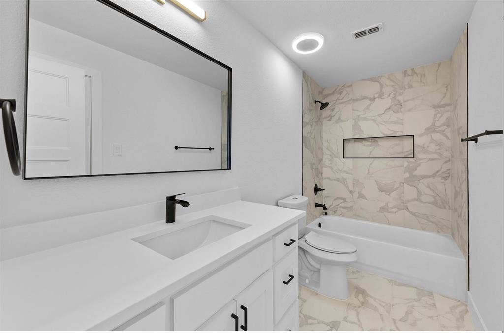 1750 Greenwood Court, Prosper, TX 75078 Contemporary bathroom featuring a vanity with an integrated sink, matte black fixtures, a rectangular framed mirror, and a tiled tub surround with an integrated niche
