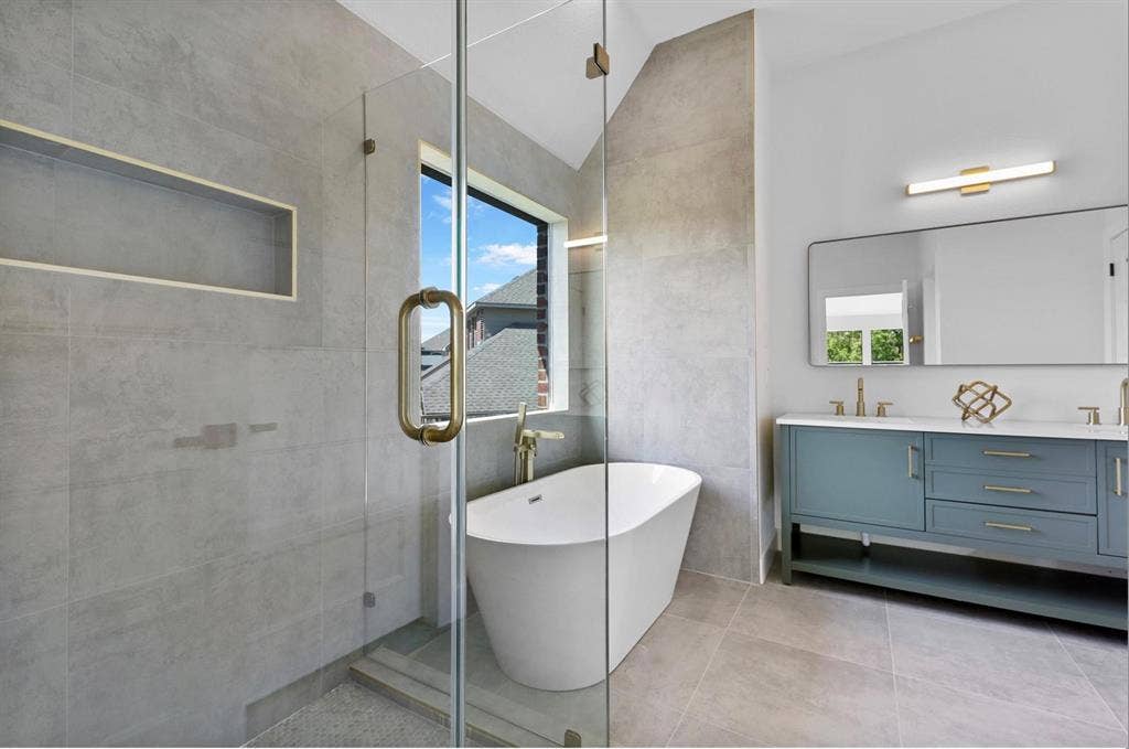 1750 Greenwood Court, Prosper, TX 75078 Glass-enclosed shower with a built-in niche, freestanding bathtub, dual vanity with white countertop, and gold-finish fixtures