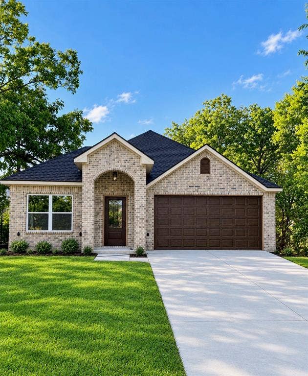 406 E Belknap Street, Ennis, TX 75119 Exterior facade featuring light-toned brick masonry, an arched entryway, a dark shingled roof, a double-car garage, and a concrete driveway