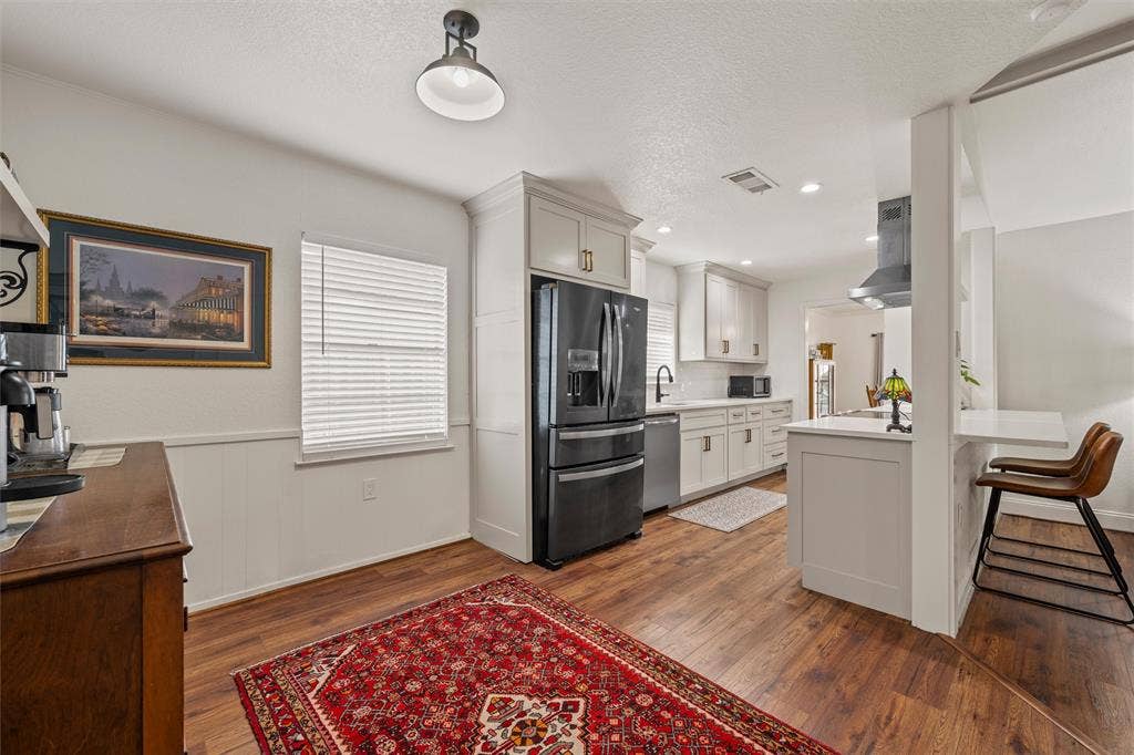 1712 Laurel Lake Drive, Waco, TX 76710 Wood-finish flooring, white cabinetry, integrated black appliances, pendant lighting, and a breakfast bar