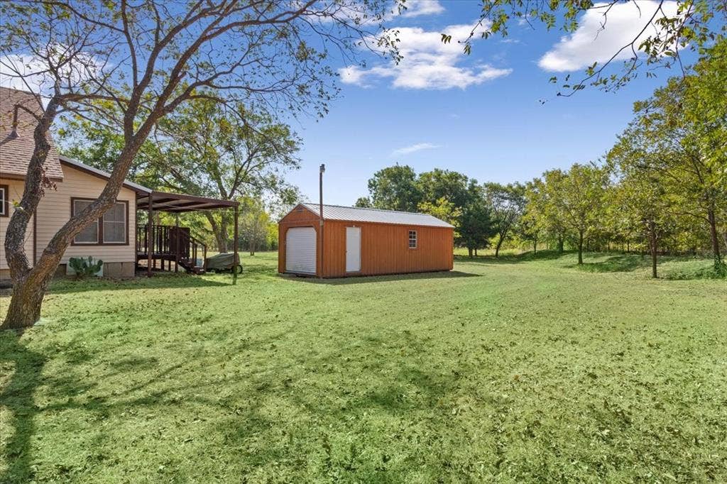 4246 Old Caufield Ranch Road, McGregor, TX 76657 Expansive lawn area with a detached storage shed, covered porch, and mature trees