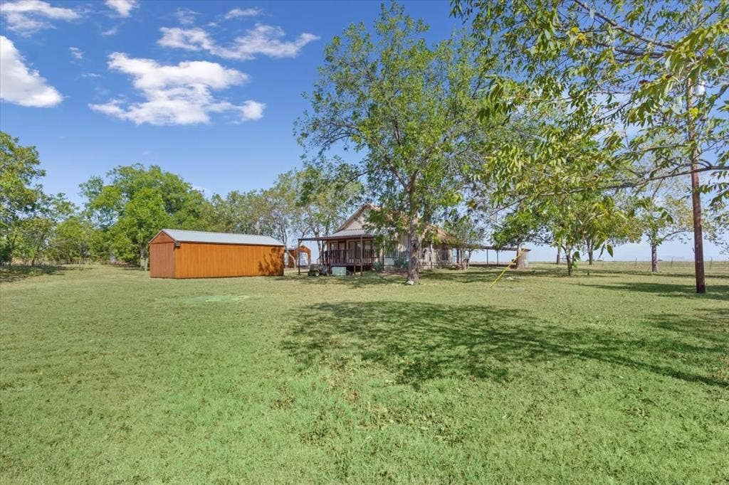 4246 Old Caufield Ranch Road, McGregor, TX 76657 Expansive green grounds featuring mature trees and a detached storage building with a metal roof