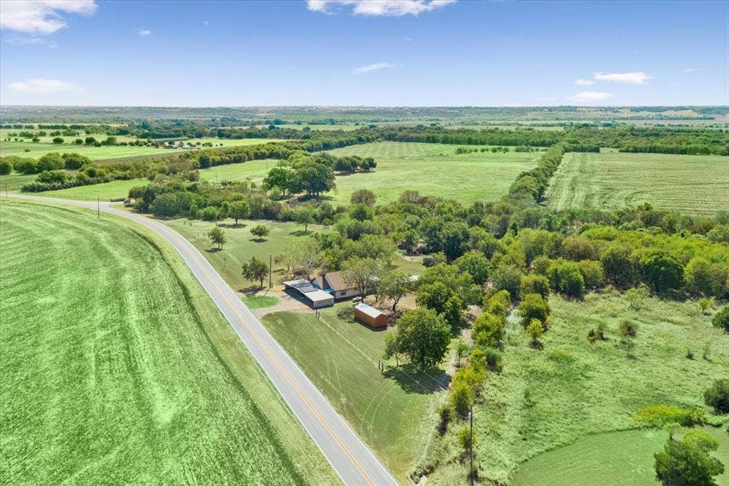 4246 Old Caufield Ranch Road, McGregor, TX 76657 Expansive green fields, mature trees, a long paved road, and a single-story residence
