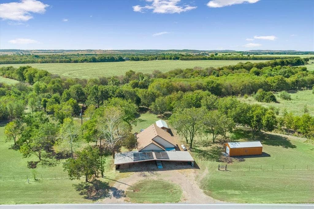 4246 Old Caufield Ranch Road, McGregor, TX 76657 Expansive property featuring a single-story residence, a detached storage building, a covered carport, mature trees, and open fields