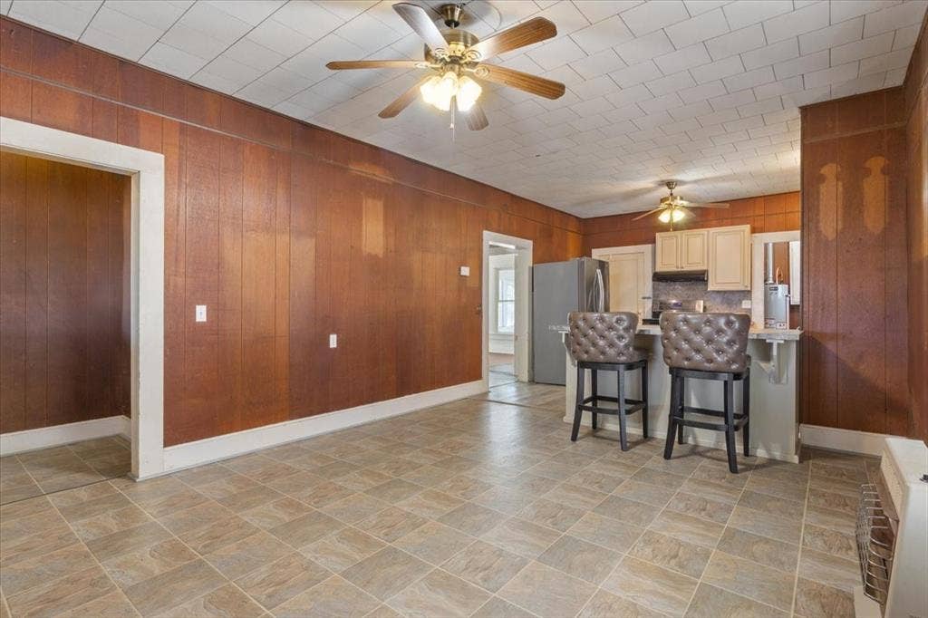 4246 Old Caufield Ranch Road, McGregor, TX 76657 Wood paneling walls, neutral tile flooring, kitchen featuring a breakfast bar, cream cabinetry, and stainless steel refrigerator