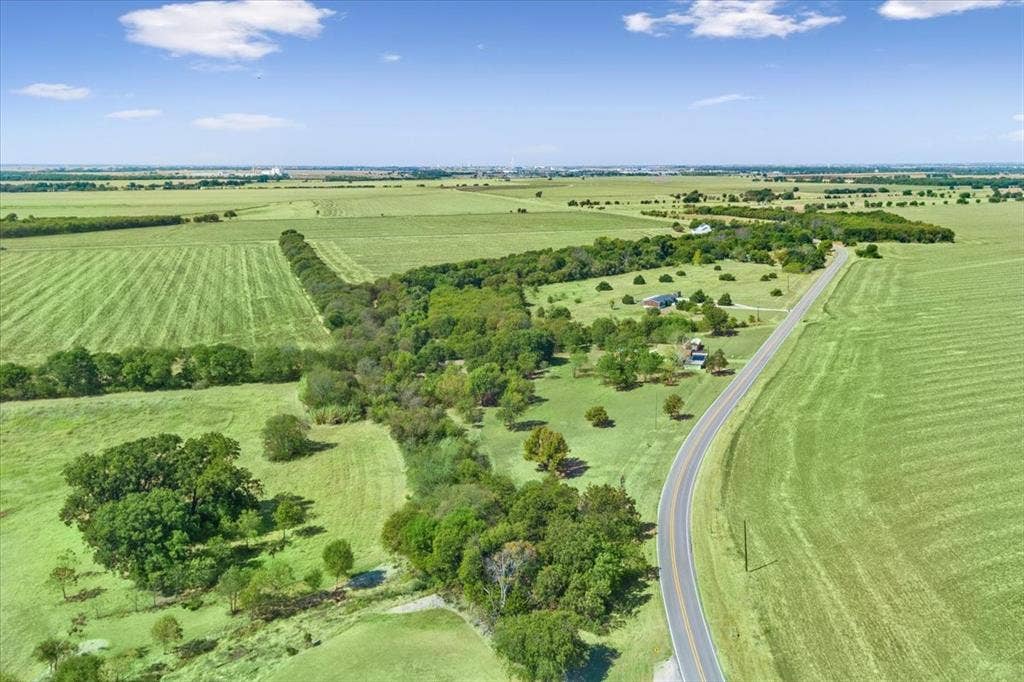 4246 Old Caufield Ranch Road, McGregor, TX 76657 Expansive green fields, a paved road, scattered mature trees, and a distant treeline
