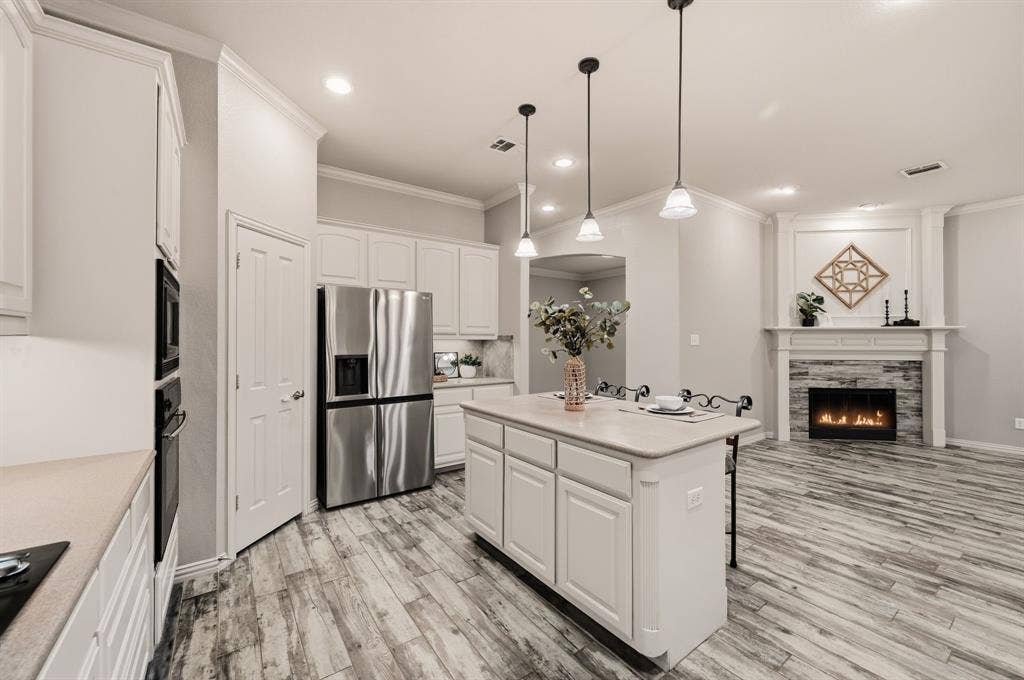 307 Park Haven Boulevard, Euless, TX 76039 Kitchen island with pendant lighting, stainless steel appliances, wood-finish flooring, white cabinetry, and a fireplace with a stone surround