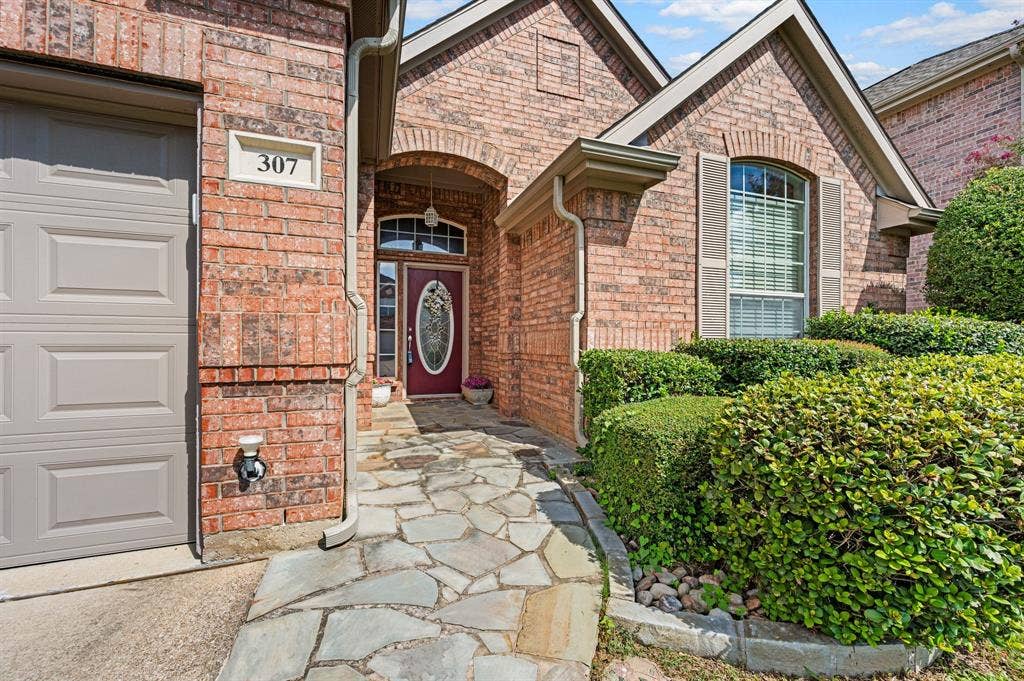 307 Park Haven Boulevard, Euless, TX 76039 Brick exterior with a stone-finish walkway, arched entry, decorative front door, and garage access