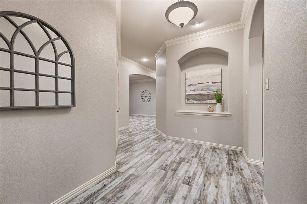 307 Park Haven Boulevard, Euless, TX 76039 Elegant hallway showcasing wood-finish plank flooring with gray and white tonal variation, arched architectural alcove with decorative window treatment, recessed ceiling lighting, and geometric wall mirror accent
