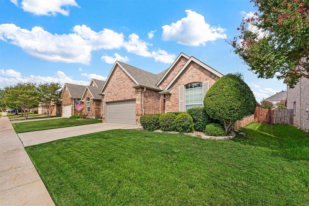 307 Park Haven Boulevard, Euless, TX 76039 Brick exterior with shutters, an arched window, an attached garage, and a manicured lawn with mature landscaping