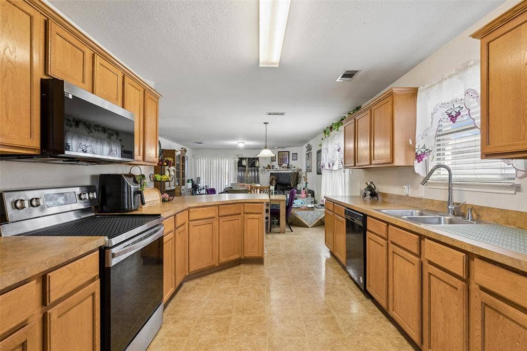 3118 Rosslynn Court, Seagoville, TX 75159 Kitchen featuring wood cabinetry, stainless steel appliances, a dual-basin sink, and tile flooring
