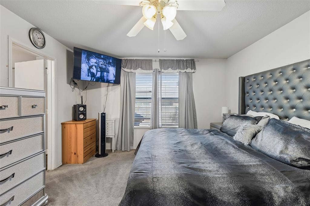 3118 Rosslynn Court, Seagoville, TX 75159 Carpeted room with a ceiling fan, two windows featuring blinds and curtains, and a tufted headboard
