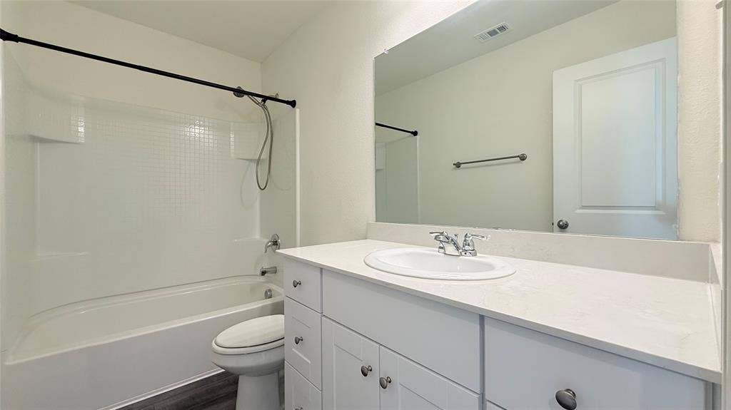 613 Delaware Avenue, Princeton, TX 75407 White vanity with an integrated sink and chrome faucet, large frameless mirror, and a white bathtub/shower combination with a black shower rod