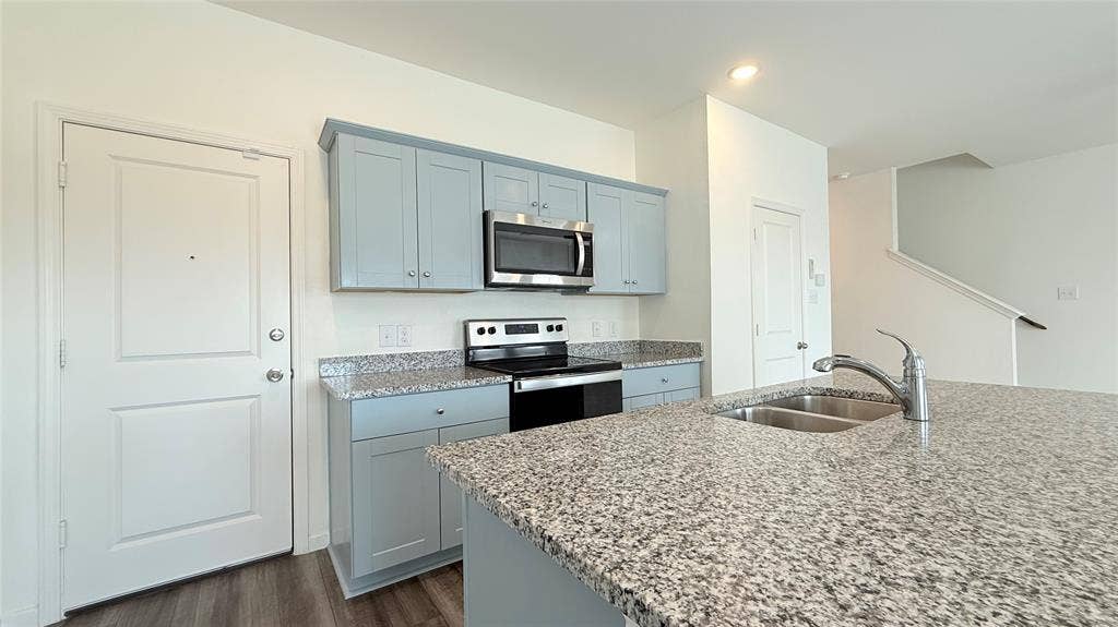 613 Delaware Avenue, Princeton, TX 75407 Kitchen featuring light blue cabinetry, stainless steel microwave, electric range, and speckled countertops