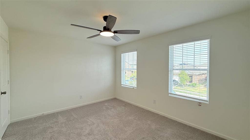 613 Delaware Avenue, Princeton, TX 75407 Light-colored walls, ceiling fan with integrated lighting, two windows with blinds, and light-colored carpeting