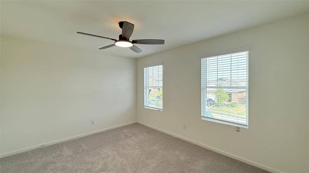 613 Delaware Avenue, Princeton, TX 75407 Neutral wall paint, ceiling fan with integrated lighting, two windows with blinds, and carpeting