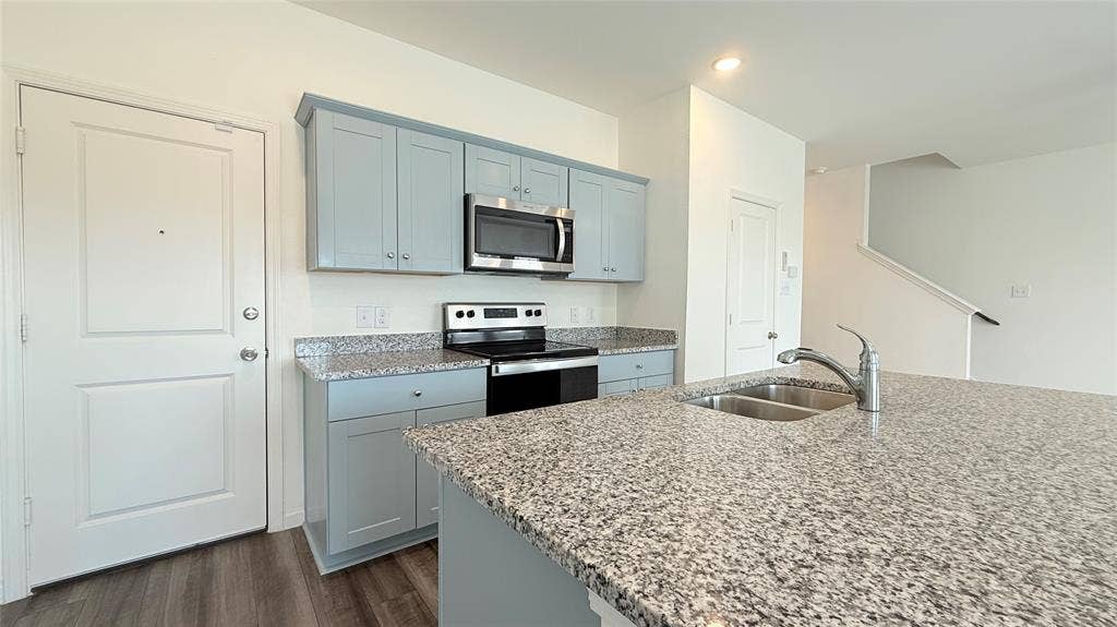 613 Delaware Avenue, Princeton, TX 75407 Kitchen featuring a dual basin sink, integrated oven range, built-in microwave, and light-colored cabinetry with a stone-finish countertop