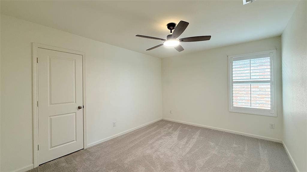 613 Delaware Avenue, Princeton, TX 75407 Neutral tone wall paint, light gray carpeting, ceiling fan with integrated lighting, paneled door, and window with plantation shutters