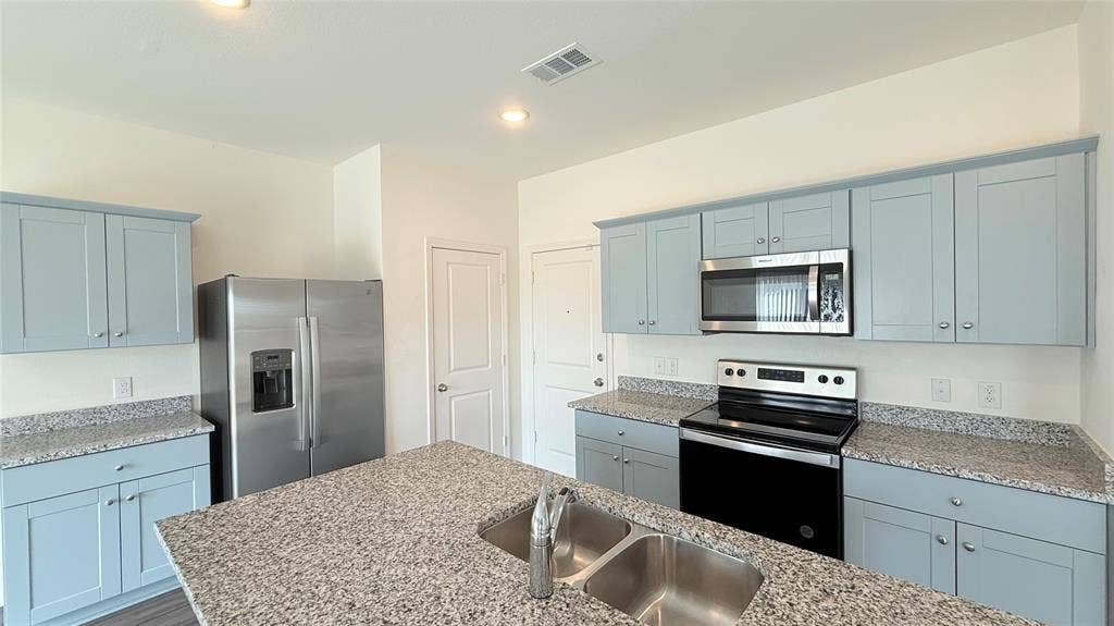 613 Delaware Avenue, Princeton, TX 75407 Kitchen with light blue cabinetry, stainless steel appliances, speckled stone countertops, and a double basin sink