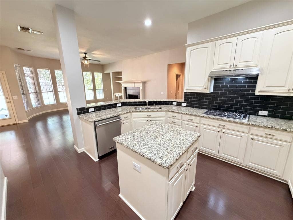 8100 Purple Martin Way, McKinney, TX 75072 Kitchen featuring a central island, stainless steel appliances, white cabinetry, dark subway tile backsplash, and light-toned countertops