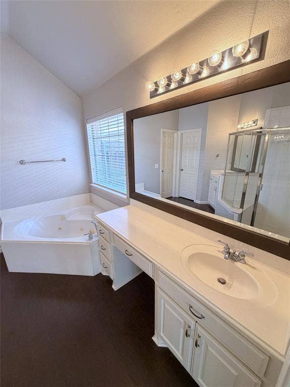 8100 Purple Martin Way, McKinney, TX 75072 Bathroom featuring a corner jetted soaking tub, dark wood-finish flooring, white vanity with integrated sink, chrome faucet, and a large wall mirror with overhead lighting