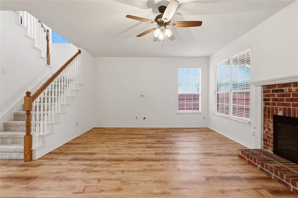 9105 Norman Drive, Plano, TX 75025 Hardwood-style flooring, brick-faced fireplace with hearth, ceiling fan with light fixture, and staircase with wood railing and carpeted treads