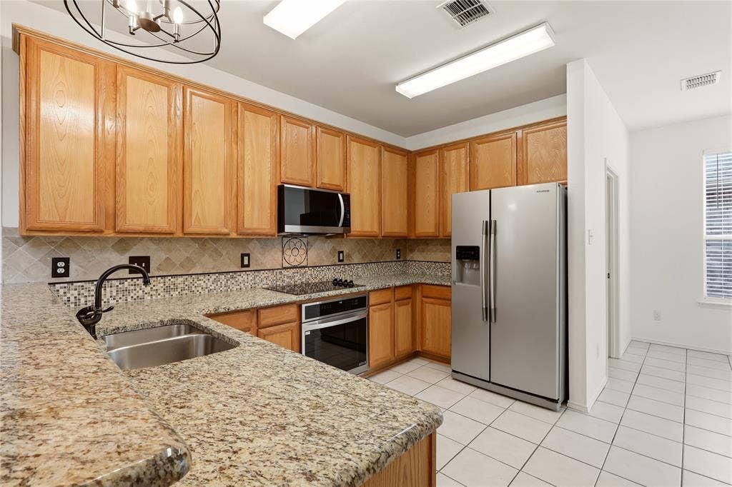 9105 Norman Drive, Plano, TX 75025 Kitchen featuring granite-style countertops, wood-finish cabinetry, stainless steel appliances, a tile backsplash, and tile flooring