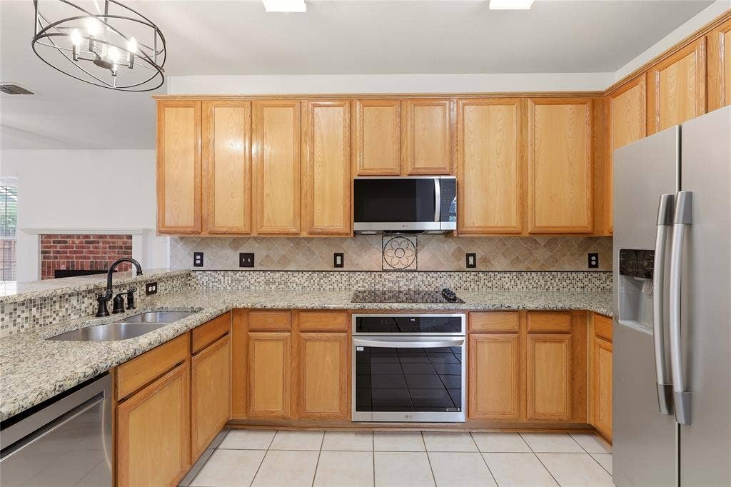 9105 Norman Drive, Plano, TX 75025 Wood cabinetry with stainless steel appliances, dual basin sink, and tile flooring