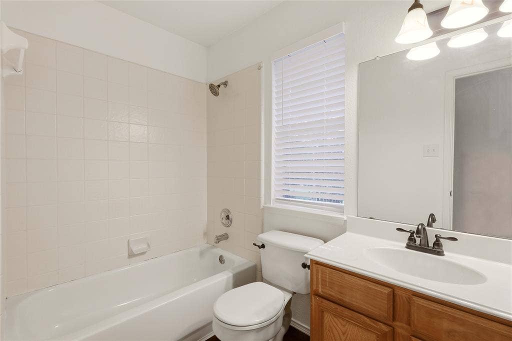 9105 Norman Drive, Plano, TX 75025 White tile bathtub surround, wood-finish vanity with white countertop, and window with privacy blinds