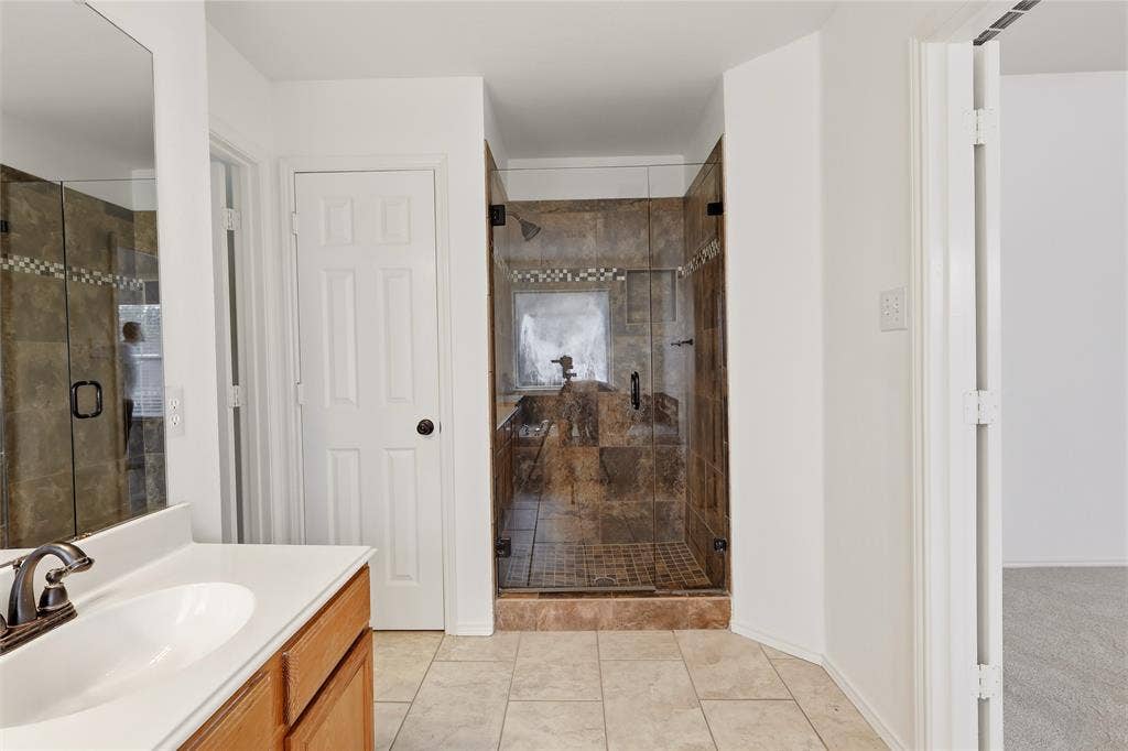 9105 Norman Drive, Plano, TX 75025 Spacious bathroom featuring a glass-enclosed shower with tiled walls and floor, a single vanity with a white countertop, and tiled flooring