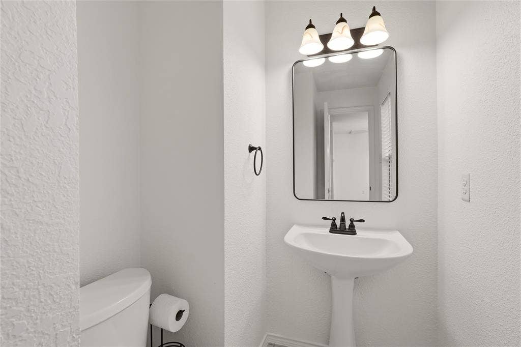9105 Norman Drive, Plano, TX 75025 Pedestal sink with dark bronze faucet, framed mirror, and three-light vanity fixture