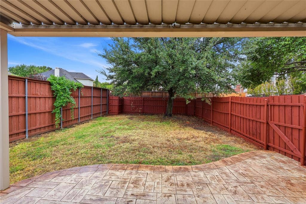 9105 Norman Drive, Plano, TX 75025 Covered patio with stamped concrete flooring, red-stained privacy fence, and mature tree