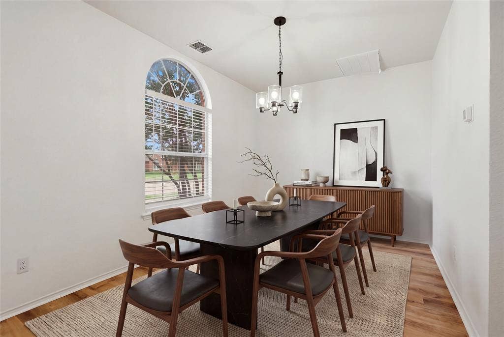 9105 Norman Drive, Plano, TX 75025 Arched window with blinds, wood-finish flooring, and a contemporary chandelier. Virtually staged.