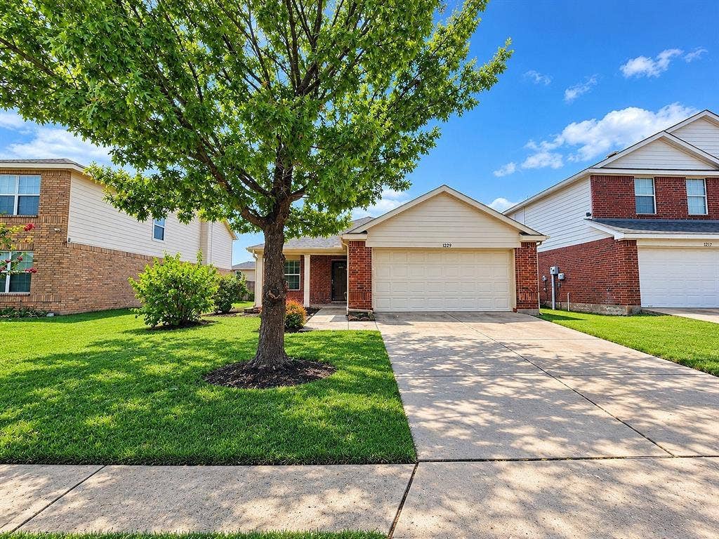 1229 Pine Forest Drive, Princeton, TX 75407 Traditional brick exterior with an attached garage, paved driveway, and mature landscaping