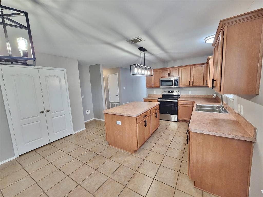 1229 Pine Forest Drive, Princeton, TX 75407 Kitchen featuring a central island, stainless steel appliances, extensive cabinetry, and neutral-toned tile flooring