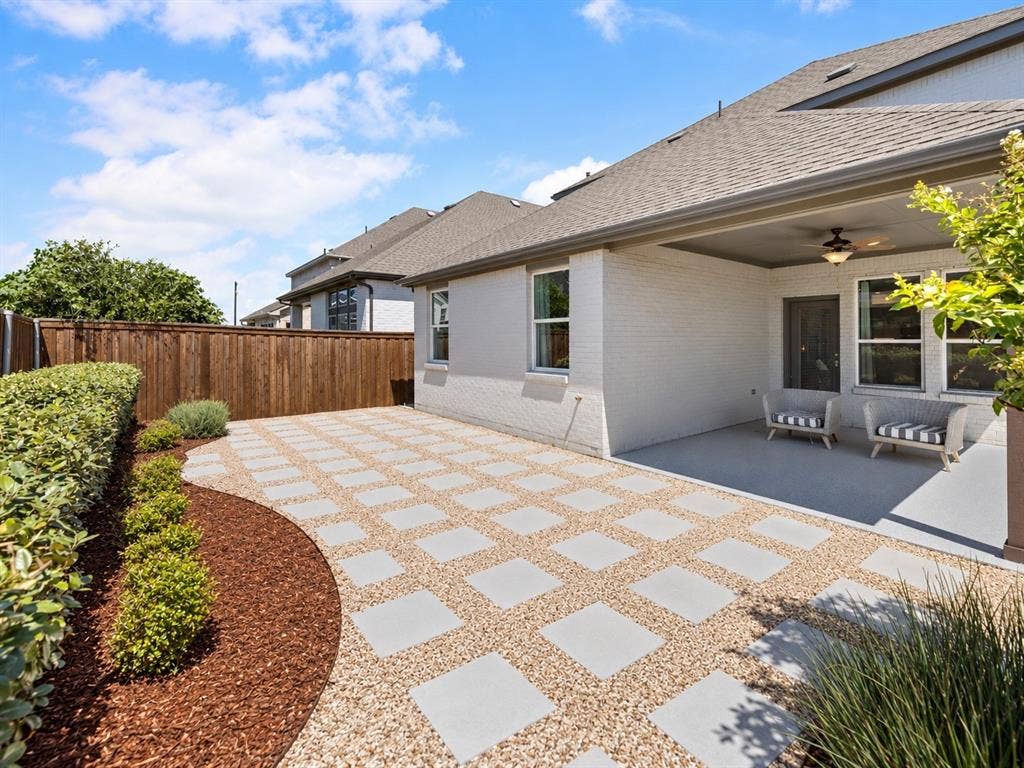 1456 Kit King Drive, Little Elm, TX 75036 Expansive outdoor patio featuring paver and gravel hardscaping, a covered porch with a ceiling fan, a private wood fence, and landscaped borders with mature greenery