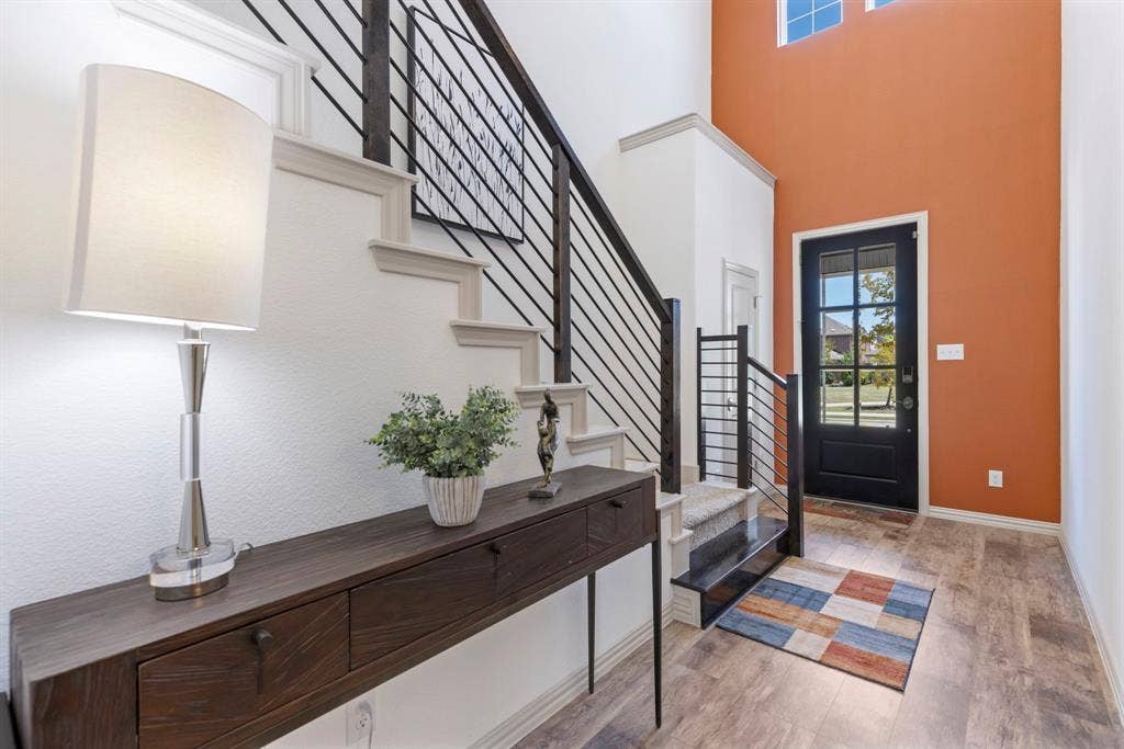 1456 Kit King Drive, Little Elm, TX 75036 Entryway featuring a high ceiling, transom windows, wood-finish flooring, a black paneled door with glass inserts, and a staircase with metal railings