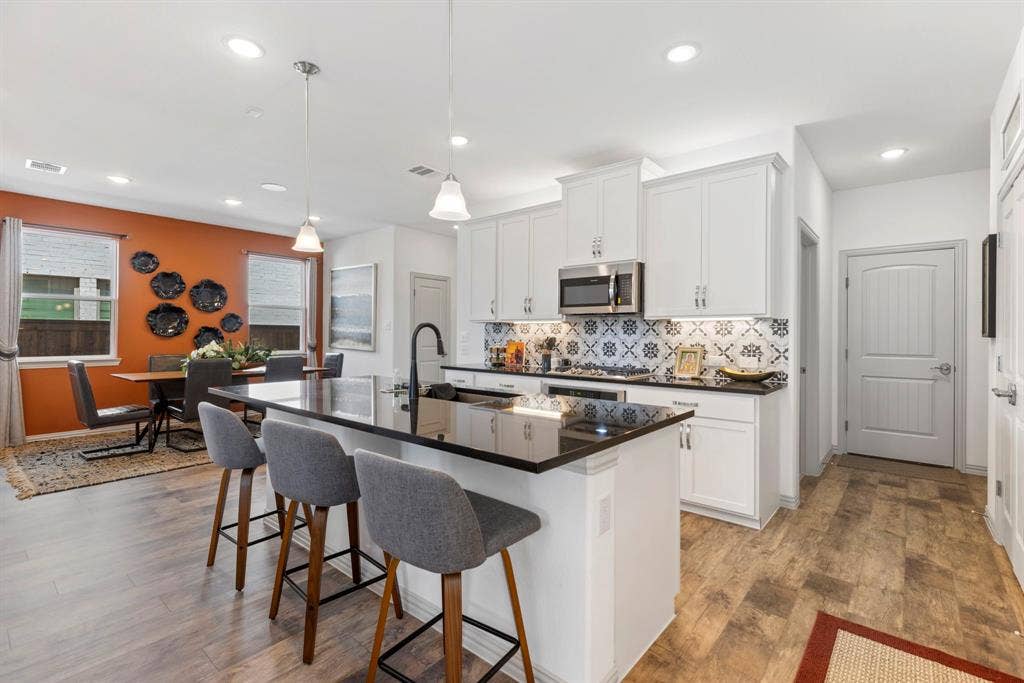 1456 Kit King Drive, Little Elm, TX 75036 Open-concept kitchen and dining area featuring white cabinetry, a large kitchen island with a black countertop, stainless steel appliances, and wood-finish flooring