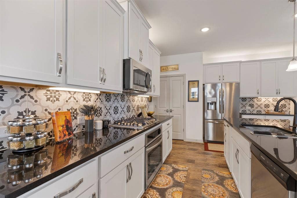 1456 Kit King Drive, Little Elm, TX 75036 White shaker cabinetry with chrome hardware, dark countertops, patterned tile backsplash, wood-finish flooring, and stainless steel appliances
