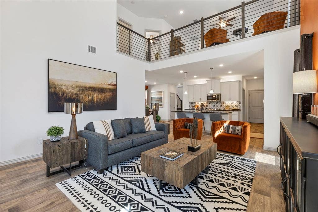 1456 Kit King Drive, Little Elm, TX 75036 Open-concept living area featuring high ceilings, wood-finish flooring, a kitchen with a patterned tile backsplash, a tiered island, and a loft with horizontal railings