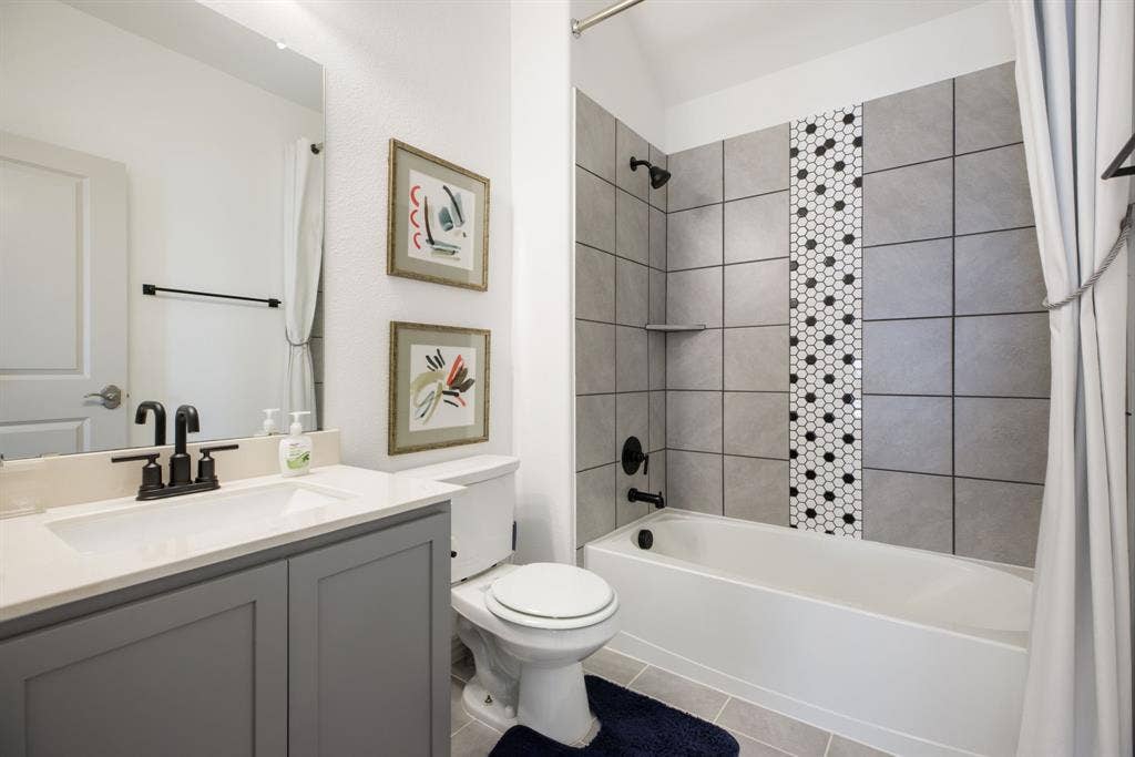 1456 Kit King Drive, Little Elm, TX 75036 Bathroom featuring a single vanity with stone countertop, matte black fixtures, and a shower/tub combination with tiled surround and decorative accent