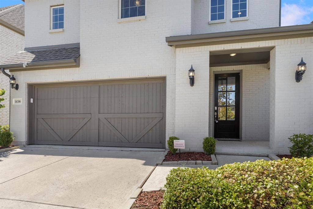 1456 Kit King Drive, Little Elm, TX 75036 Brick exterior with white finish, covered entry, black paneled front door with glass inserts, and two-car garage with decorative doors